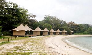 Couple dining on wooden deck of luxury glamping tent — oceanfront dinner, transparent tent sidewalls, beach resort